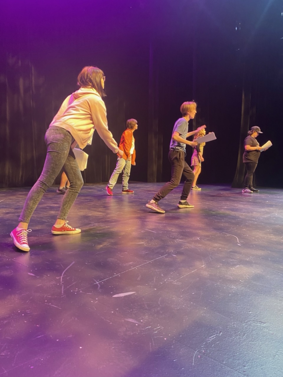 Teens are engaged in dynamic movement on stage, purple light surrounds them, 